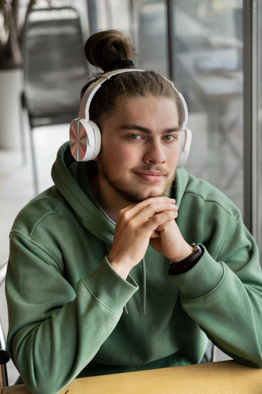 Man wearing white headphones and a green hoodie sitting at a table.