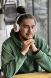 Man wearing white headphones and a green hoodie sitting at a table.